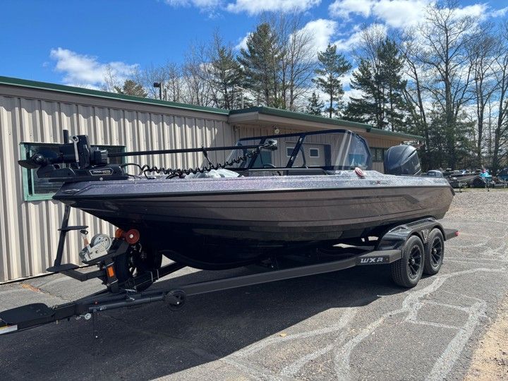 Black fishing boat on a trailer parked beside a metal building under a blue sky