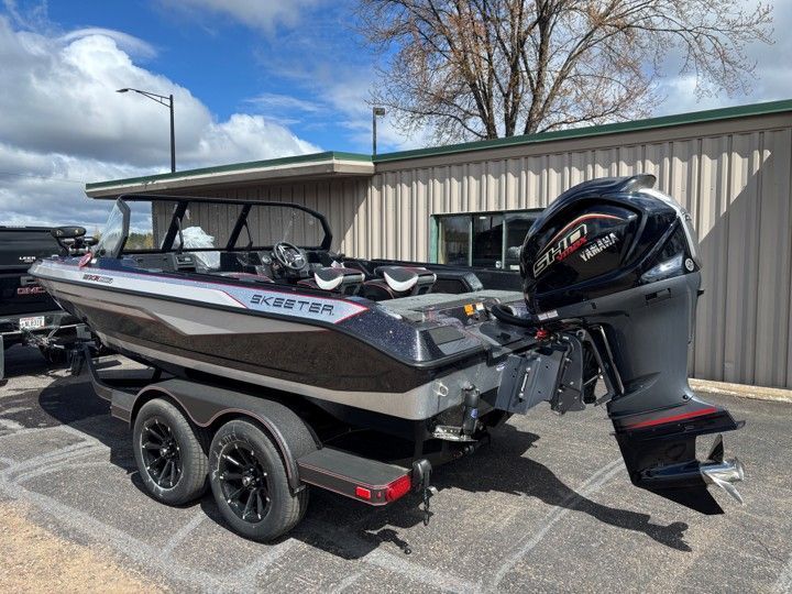 Black fishing boat on a trailer with outboard motor, parked beside a metal building under a clear sky