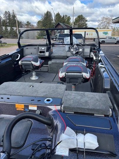 Fishing boat cockpit with two seats, steering wheel, and tackle on the deck, parked on a trailer