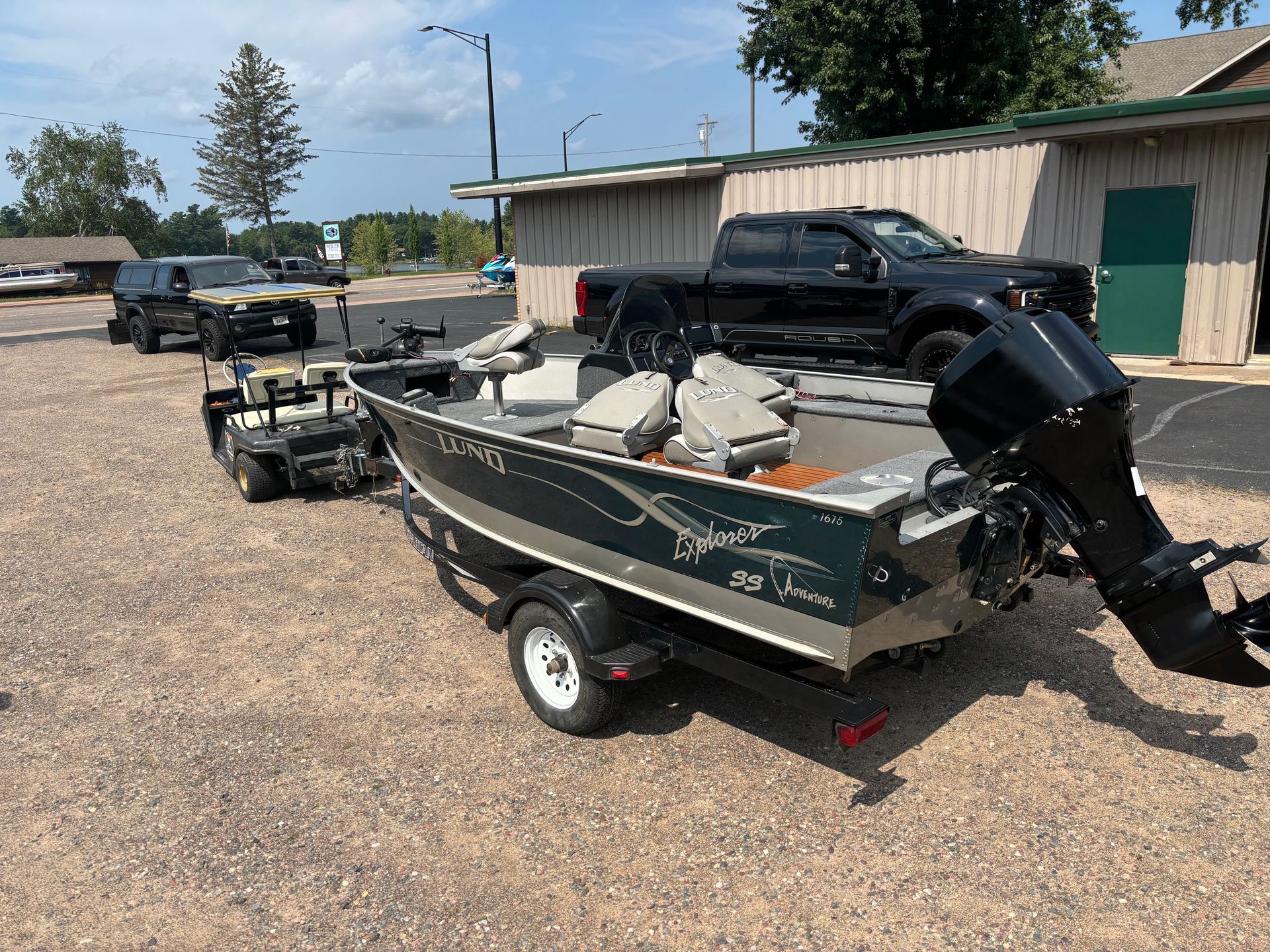 A boat is parked on a trailer in a parking lot next to a truck.