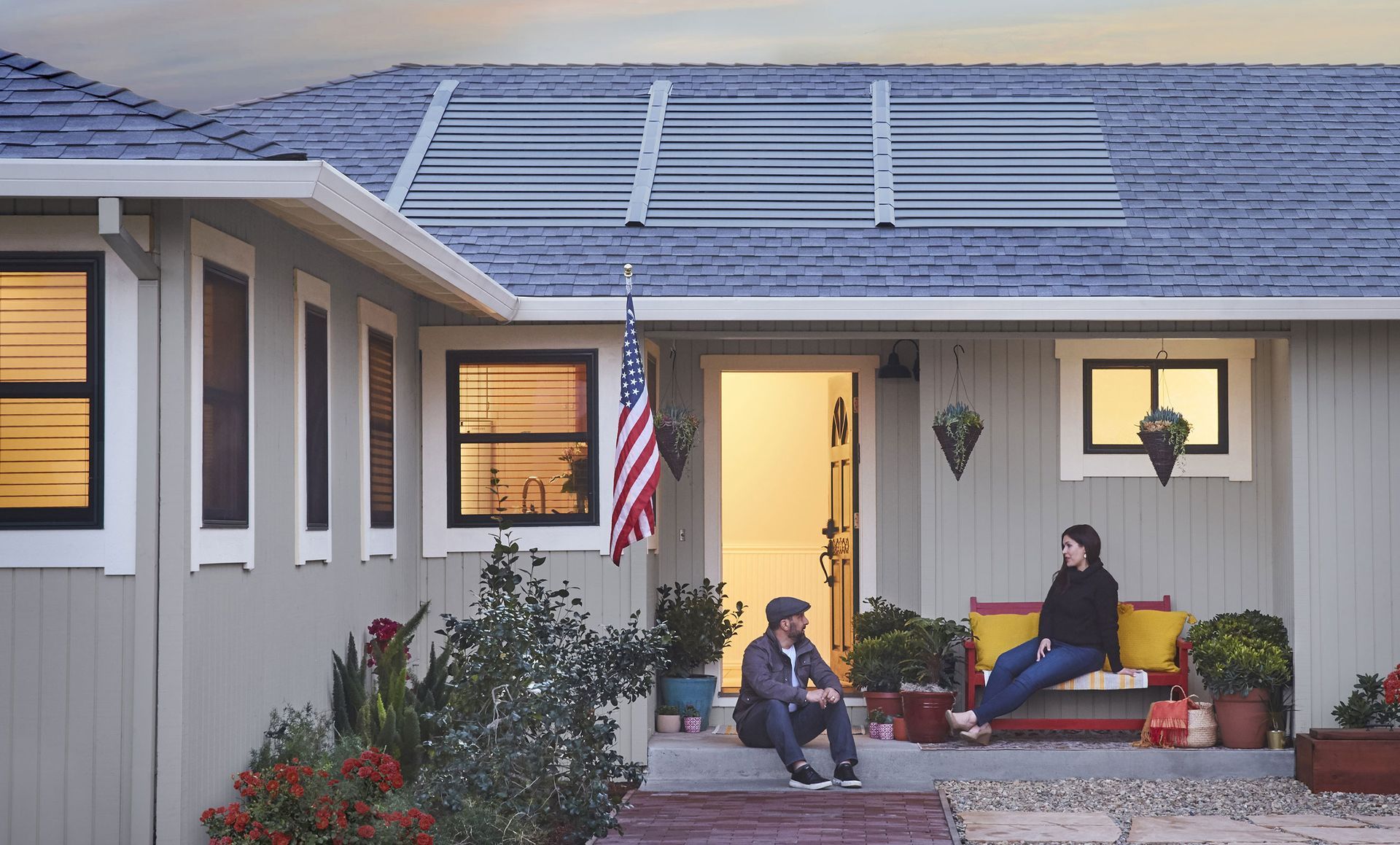 A man and a woman are sitting on the porch of a house with solar panels on the roof.