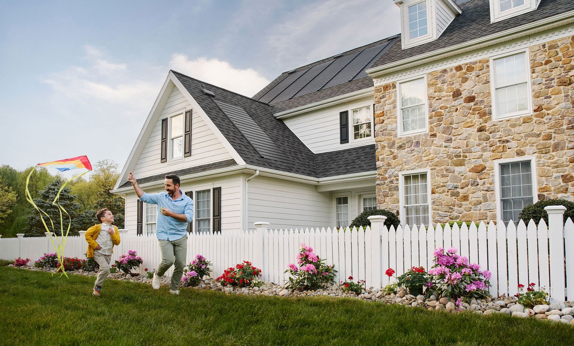 A man and a child are flying a kite in front of a house.