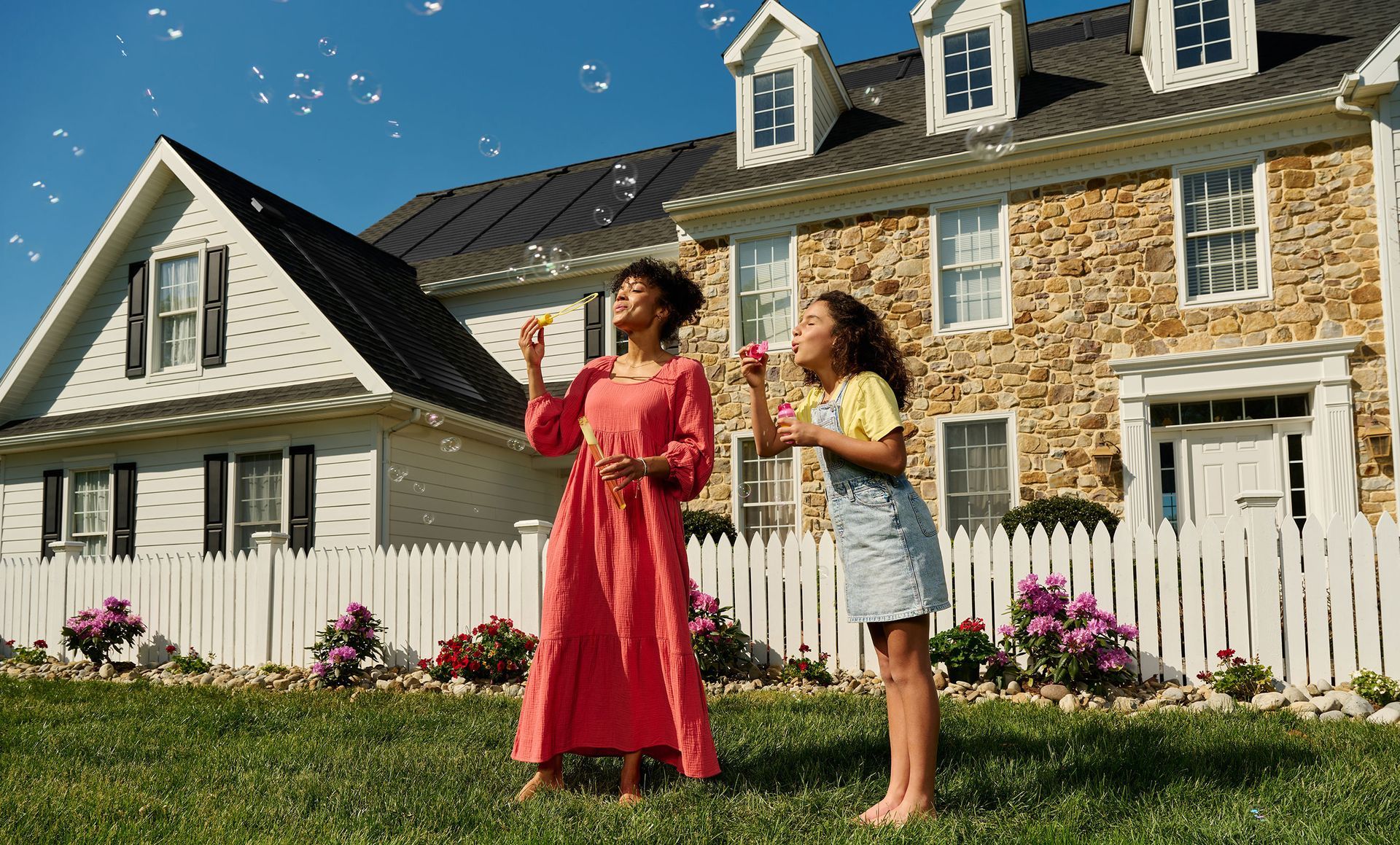 A woman and a girl are blowing soap bubbles in front of a house.