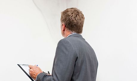 A man in a suit is holding a clipboard and a pen.