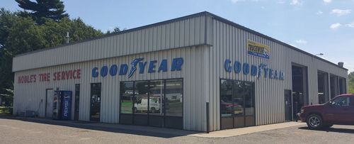 Goodyear tire service shop exterior with white siding, blue signage, and a parked red pickup truck