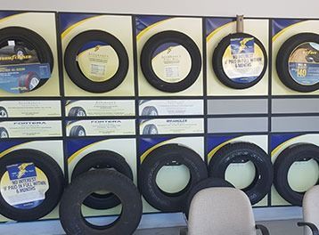 Tire display shelf with stacked black tires and blue-and-white labels in a store.
