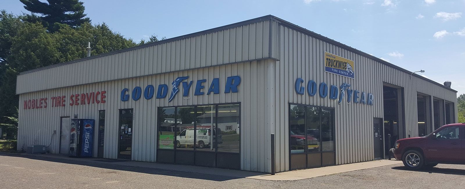 Goodyear auto service shop with white metal siding and red pickup truck parked outside