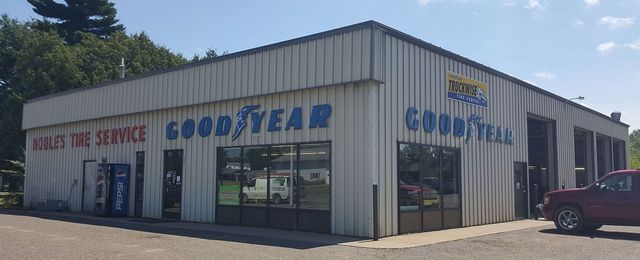 Goodyear tire shop with white metal siding and a red pickup truck parked outside