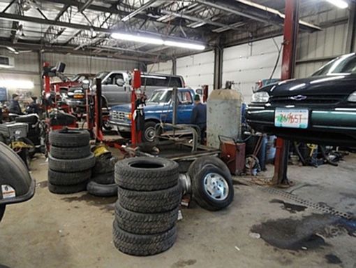 Auto repair shop with stacked tires, lifted vehicles, and car parts inside a garage