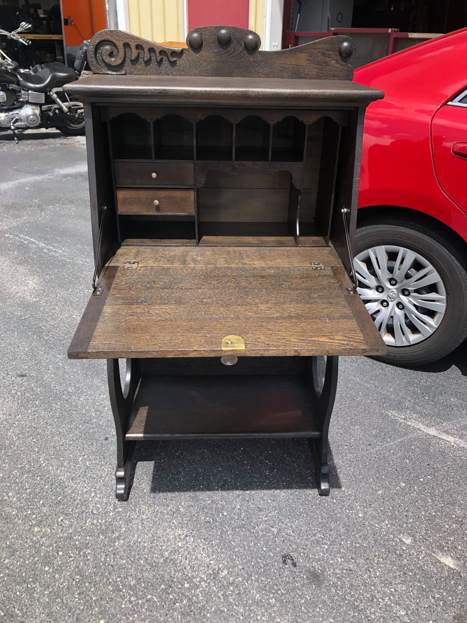 a wooden desk with the lid open is parked next to a red car