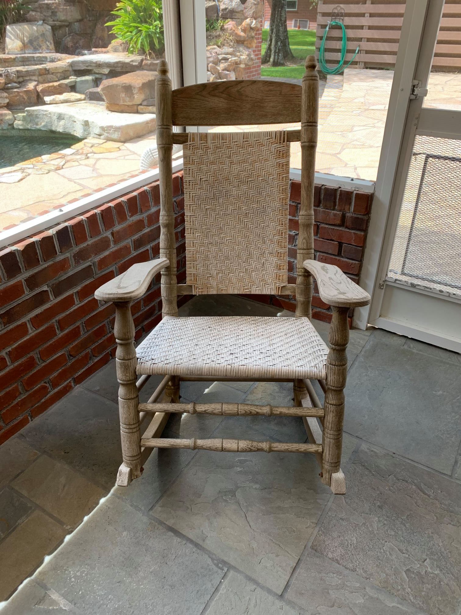a wooden rocking chair is sitting on a porch next to a brick wall