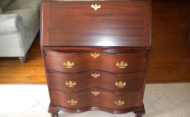 a wooden desk with three drawers is sitting on a tiled floor in a living room .