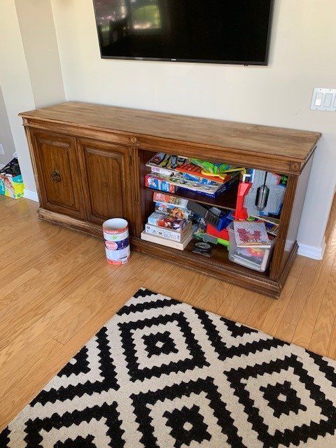 a living room with a wooden entertainment center filled with toys and a rug