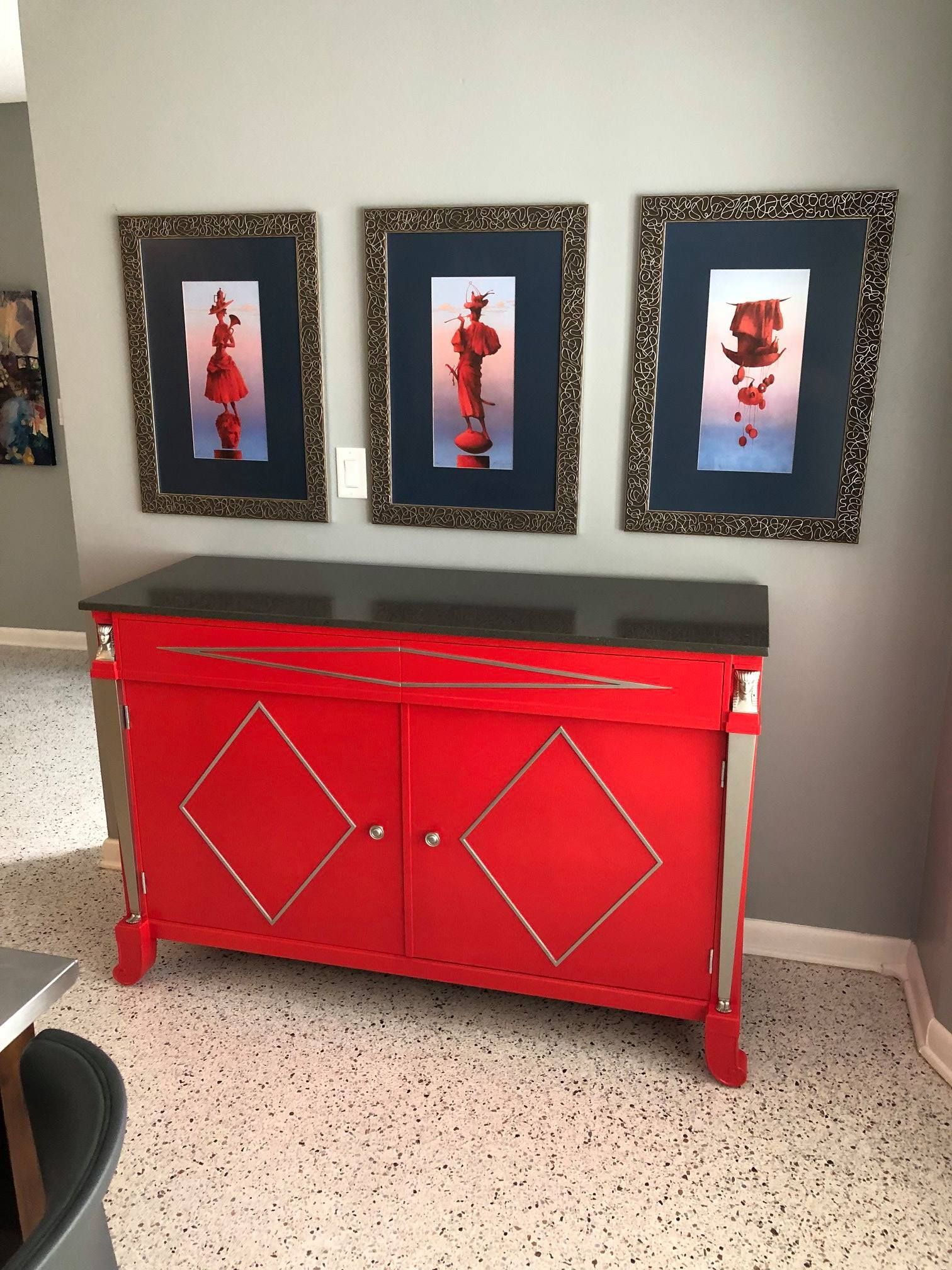 a red dresser with three pictures on the wall behind it