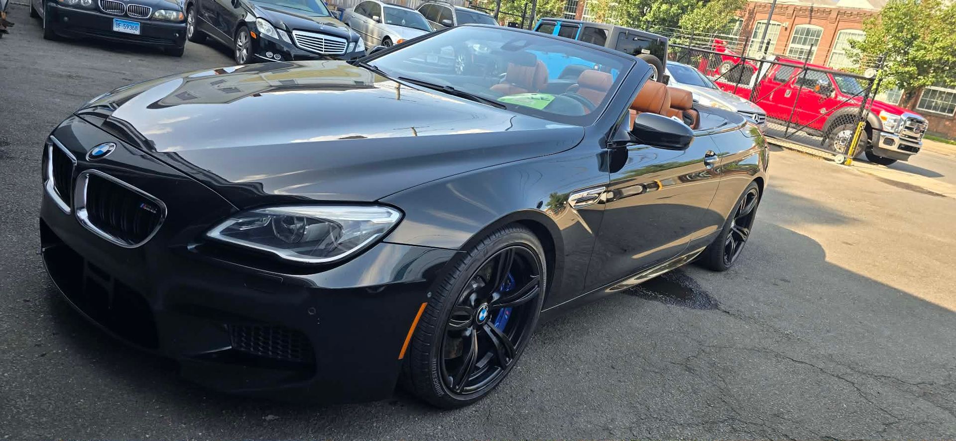 Black BMW convertible parked on a city street, with a tan interior and black wheels.