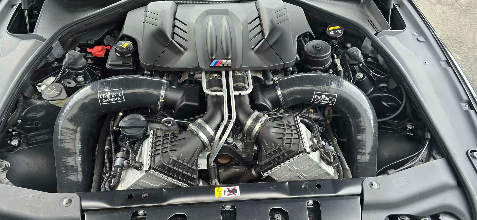 Car engine bay with exposed twin turbochargers, polished piping, and carbon-fiber cover
