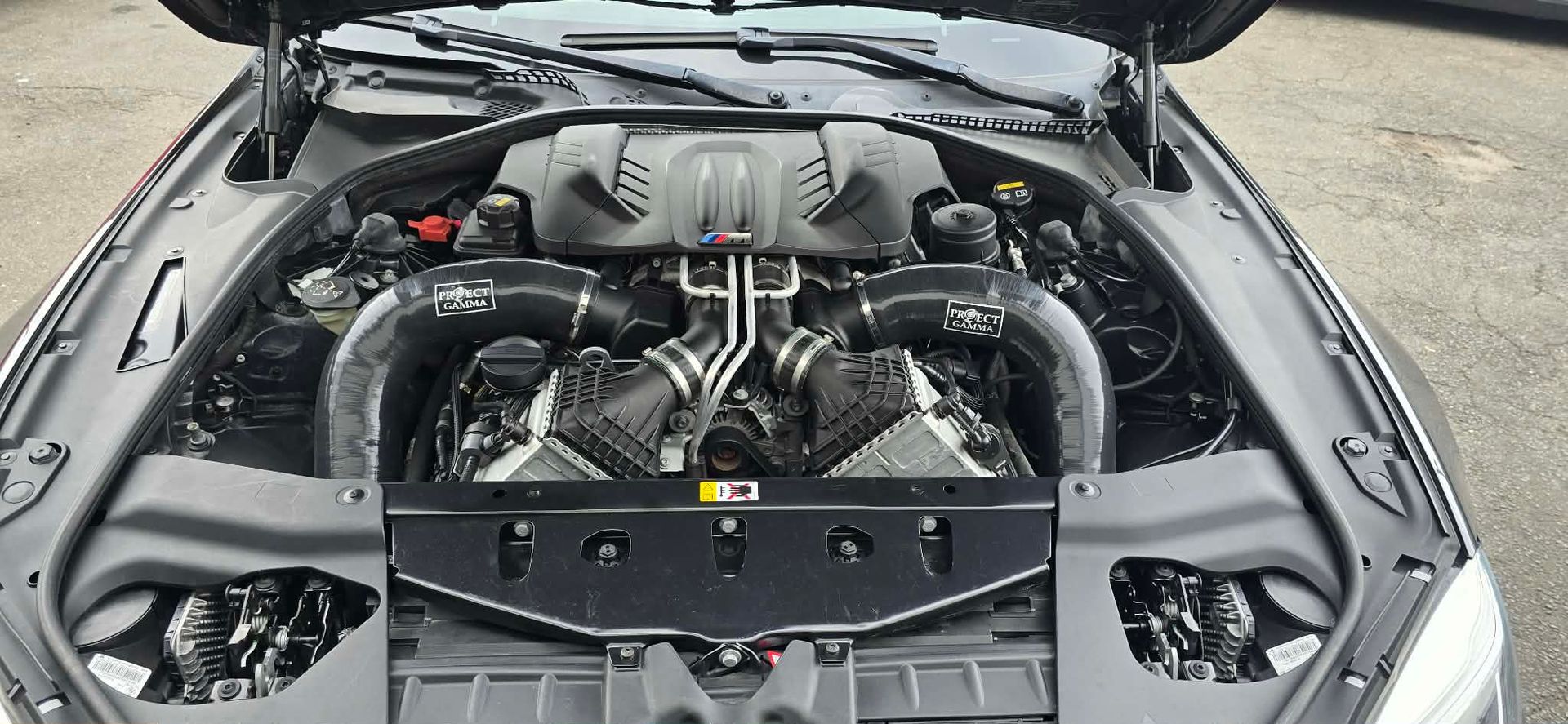 Open car hood showing a clean engine bay with chrome components and strut brace