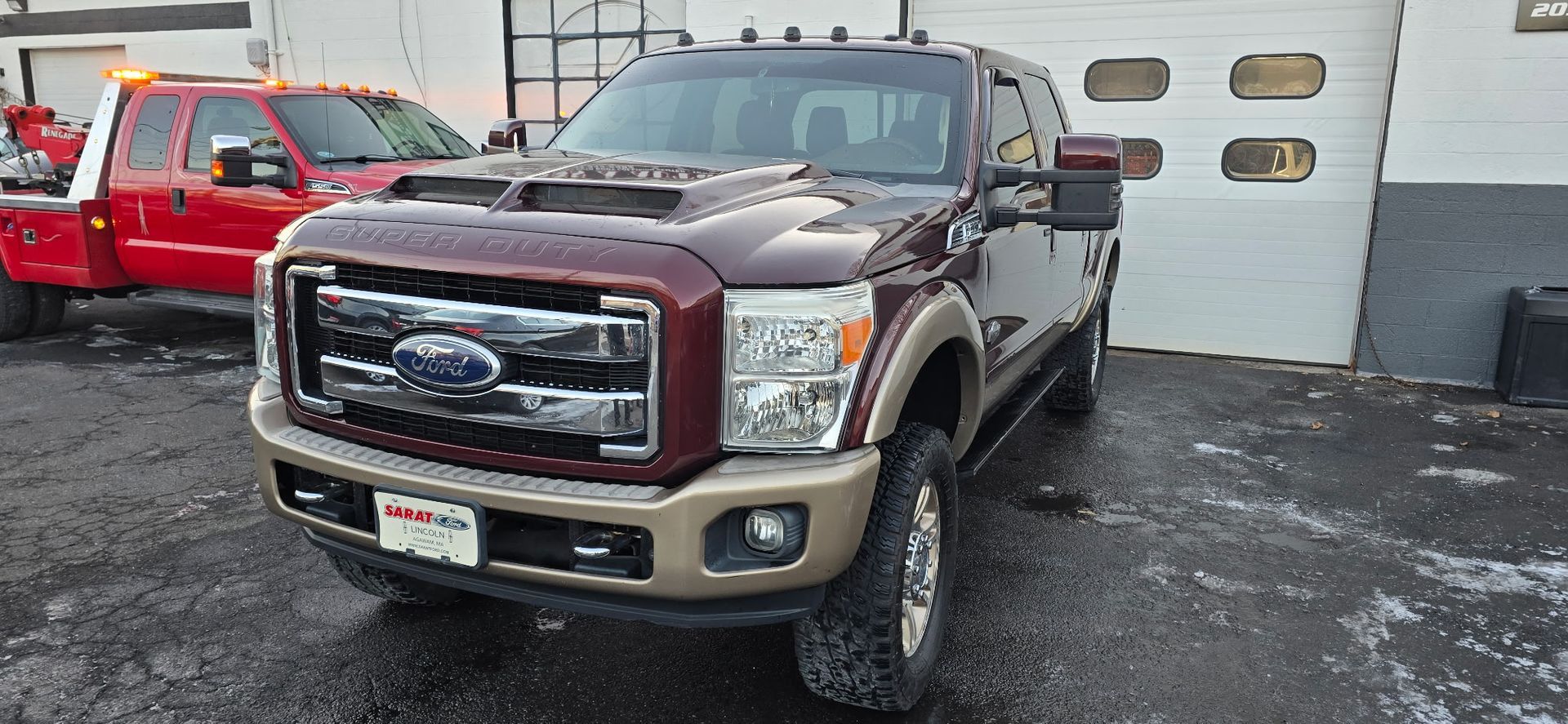Maroon and black Ford pickup parked outside an auto shop on a wet lot, with a red car beside it.