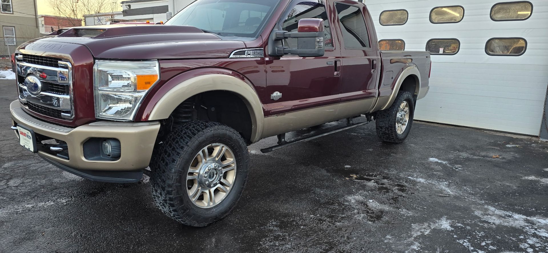 Maroon and tan pickup truck parked on pavement outside a garage door