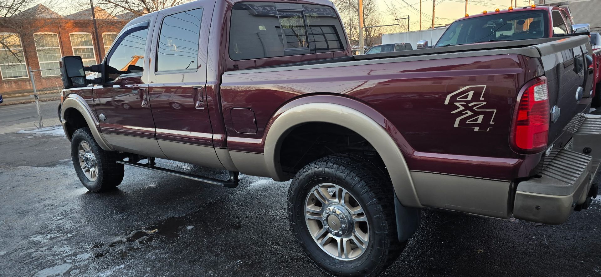 Maroon Ford pickup truck parked on a snowy roadside at sunset, rear side view