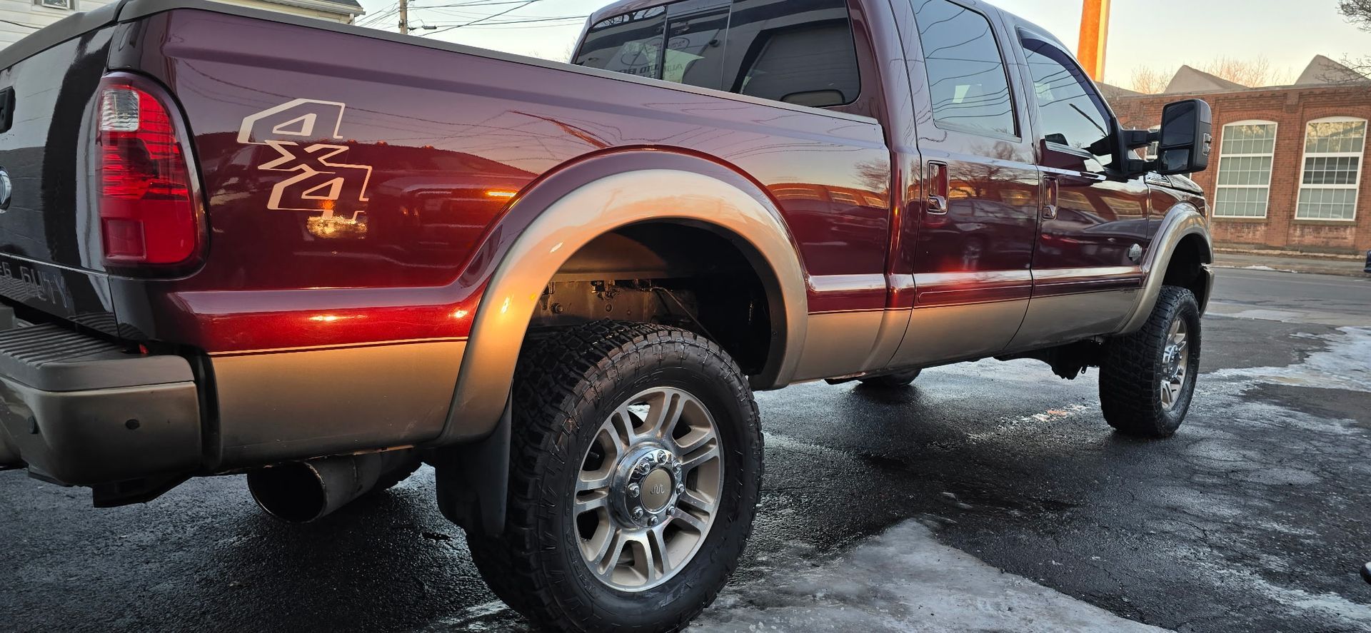 Red pickup truck parked on wet pavement at sunset, side view with chrome wheels and running boards