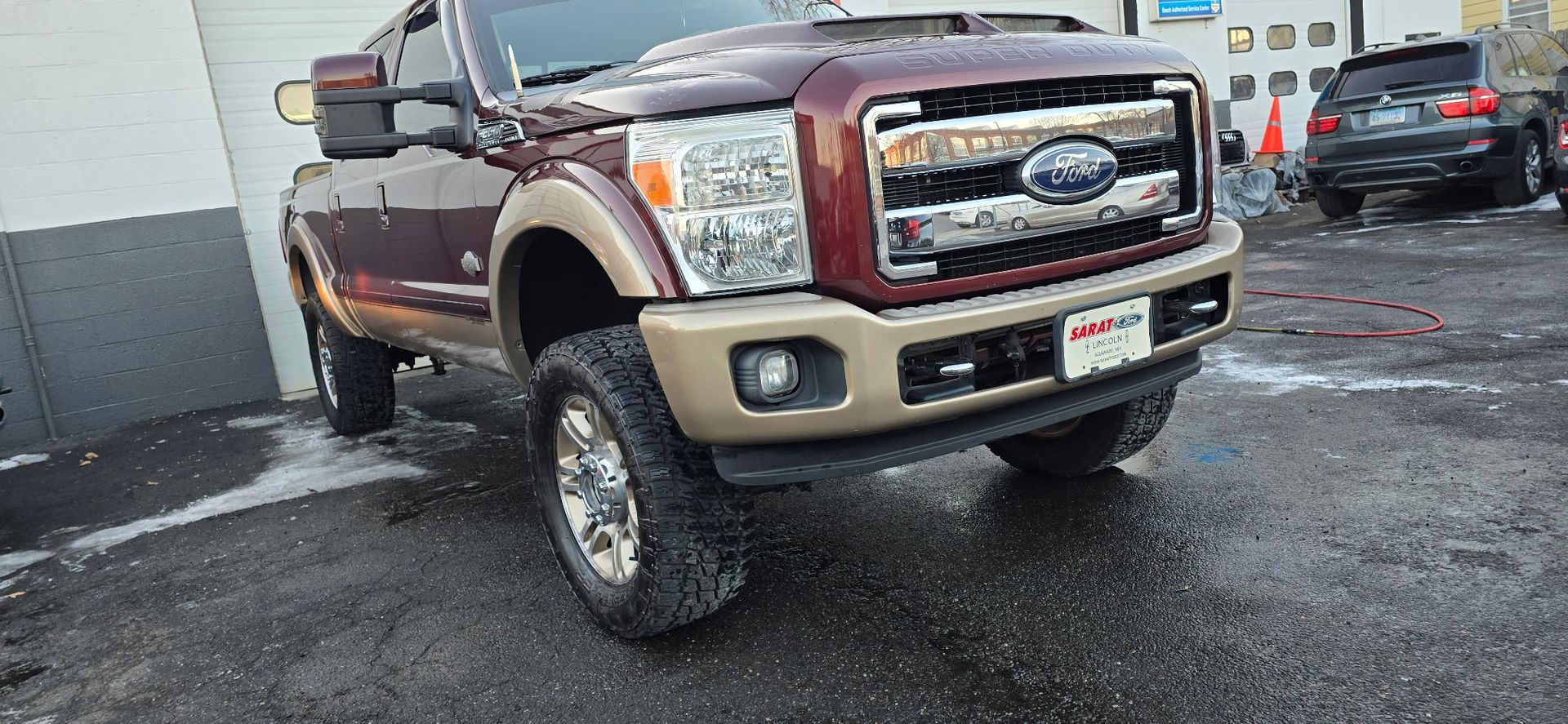 Maroon and tan Ford pickup truck parked in a wet lot on a rainy day.
