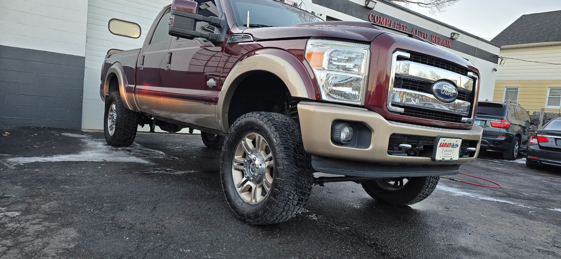 Maroon and tan lifted Ford pickup truck parked on wet pavement at a dealership lot