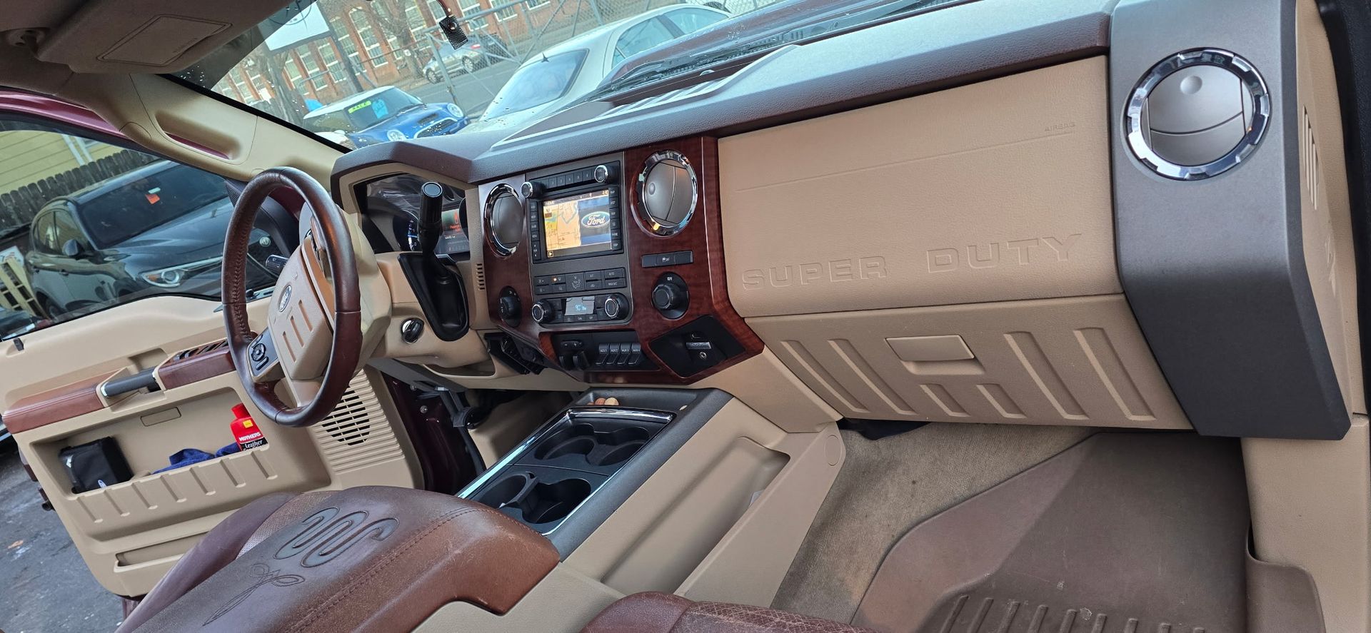 Tan and wood-trim car dashboard with steering wheel and beige seats, viewed from the passenger side