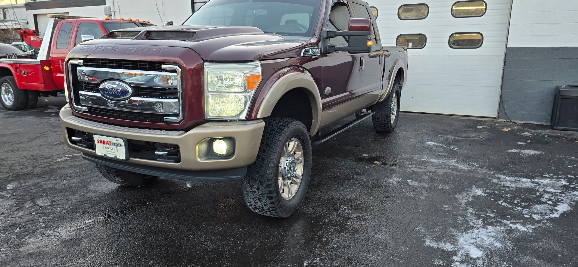 Maroon Ford pickup truck parked on a wet driveway beside a garage