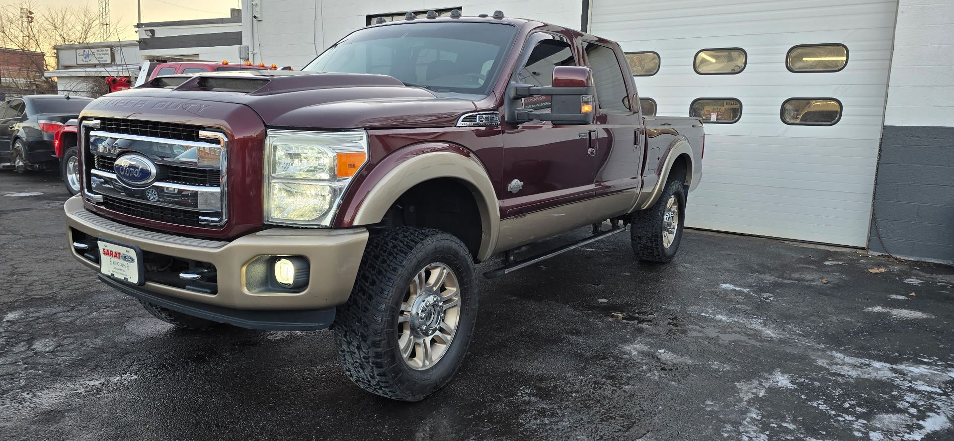 Maroon Ford Super Duty pickup truck parked on a wet driveway in front of a garage