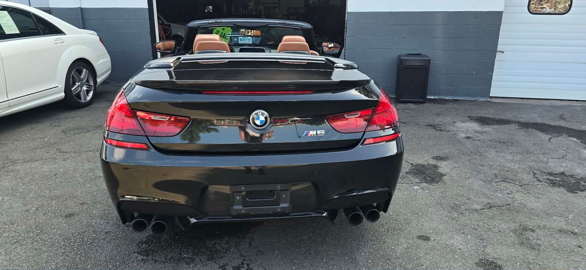 Black BMW convertible parked outdoors with its top down, rear view, at a car lot.