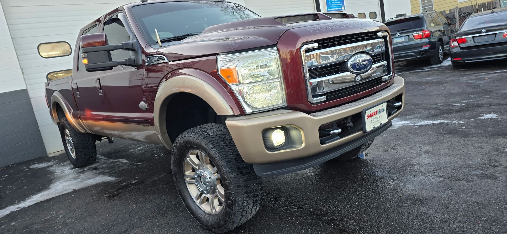 Maroon lifted Ford pickup parked on wet pavement outside a building, front angled toward camera