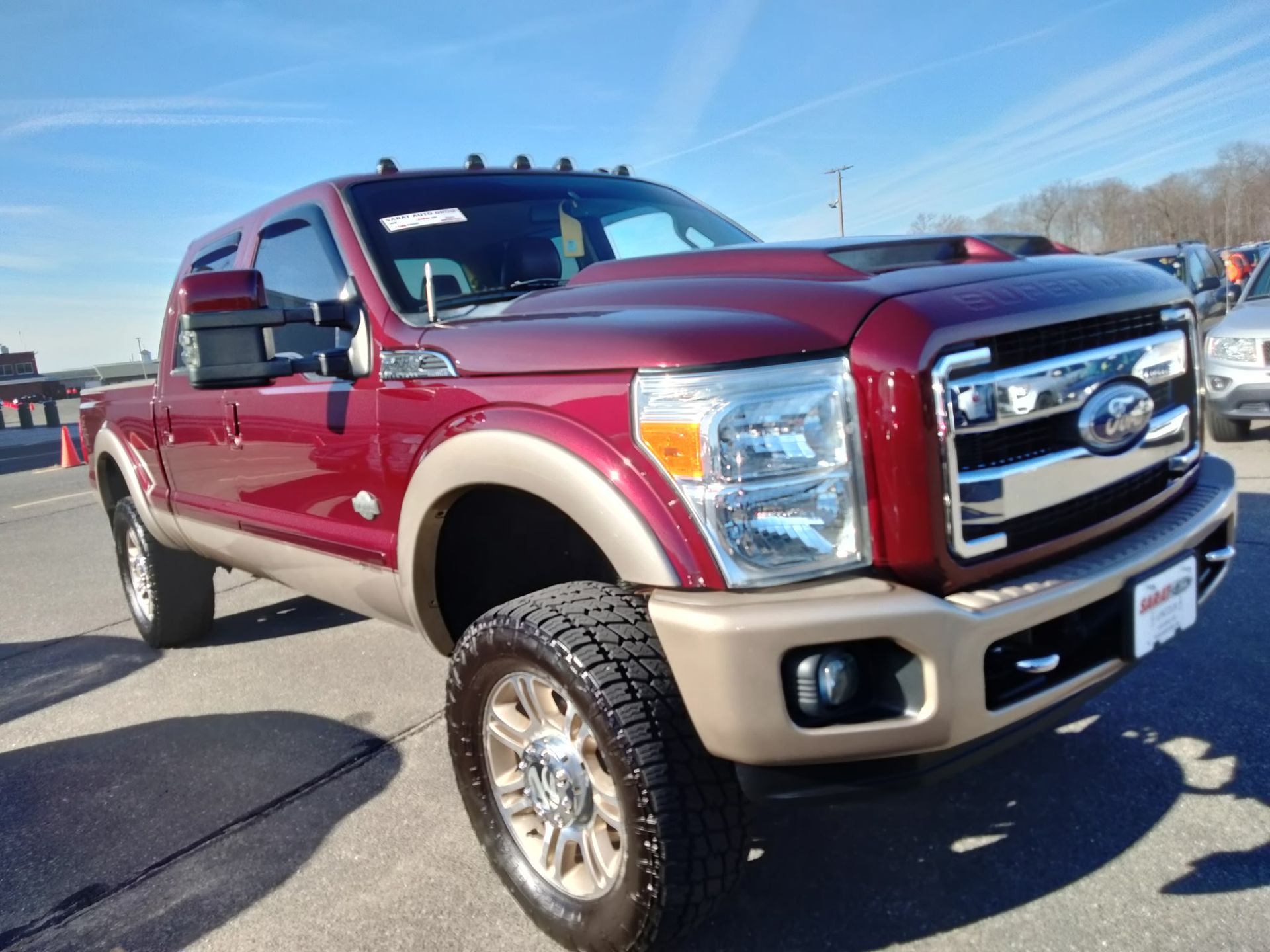 Maroon lifted Ford pickup truck parked outdoors under a clear blue sky