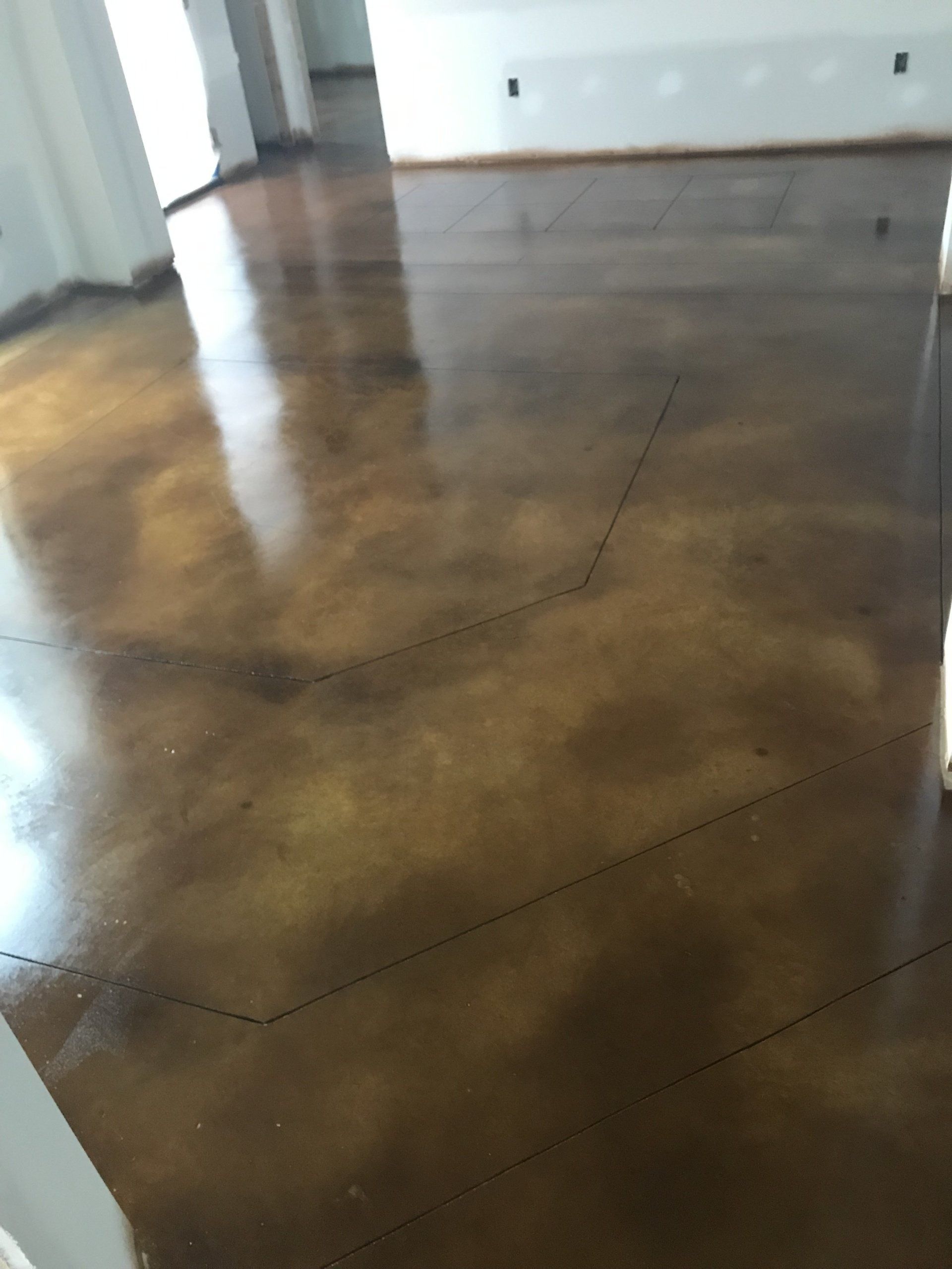Brown stained concrete floor, shiny with light reflections, black lines mark a design layout.