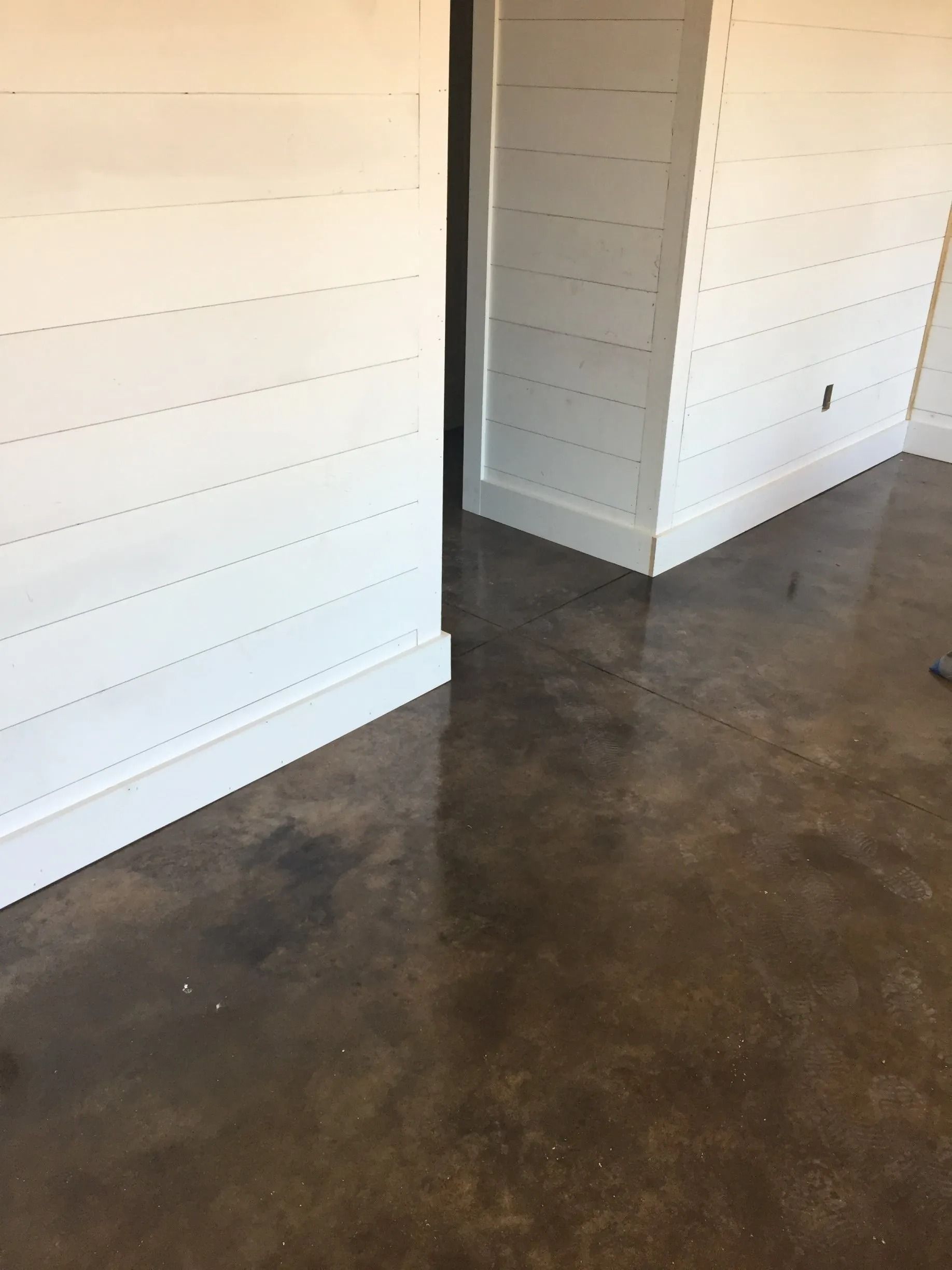 Room with white shiplap walls and a stained concrete floor.
