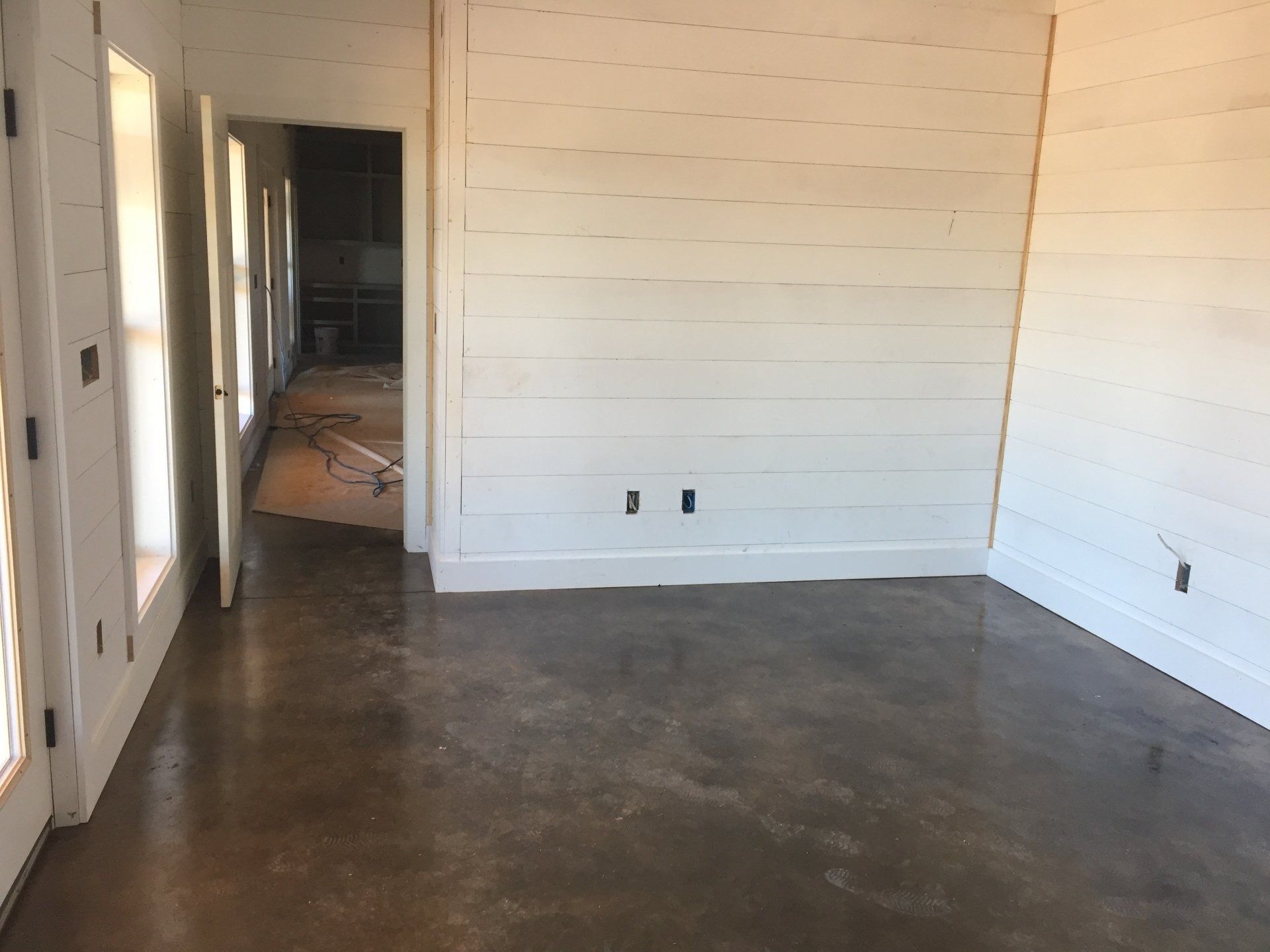 Empty room with stained concrete floor, shiplap walls, and doorway.