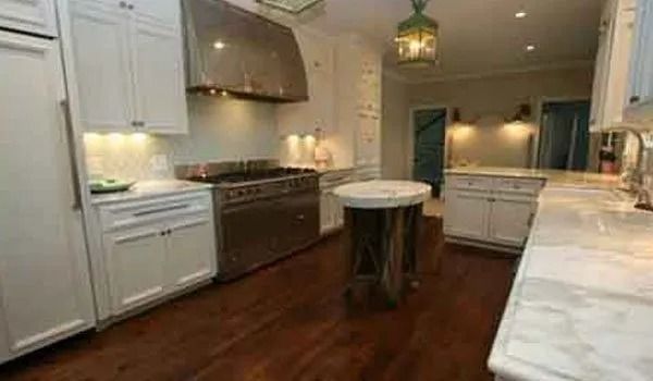 White kitchen with stainless steel appliances, dark wood floor, marble countertops, and a small island.
