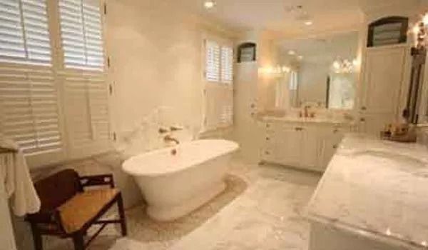 Elegant white bathroom with a freestanding bathtub, marble floors, and shutters.