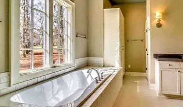 Bathroom with a large window overlooking trees, featuring a bathtub, cabinet, and sconce.