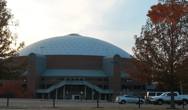 Large dome-shaped building with brick facade and trees in front; overcast sky in background.