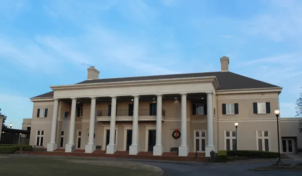 Large two-story building with white columns and light-colored walls under a blue sky.