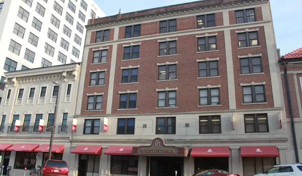 Red brick building with awnings over storefronts, next to a white building.
