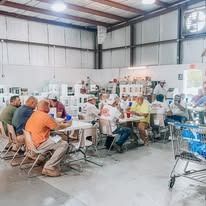 People at tables in a warehouse-like building; some working, others sitting.