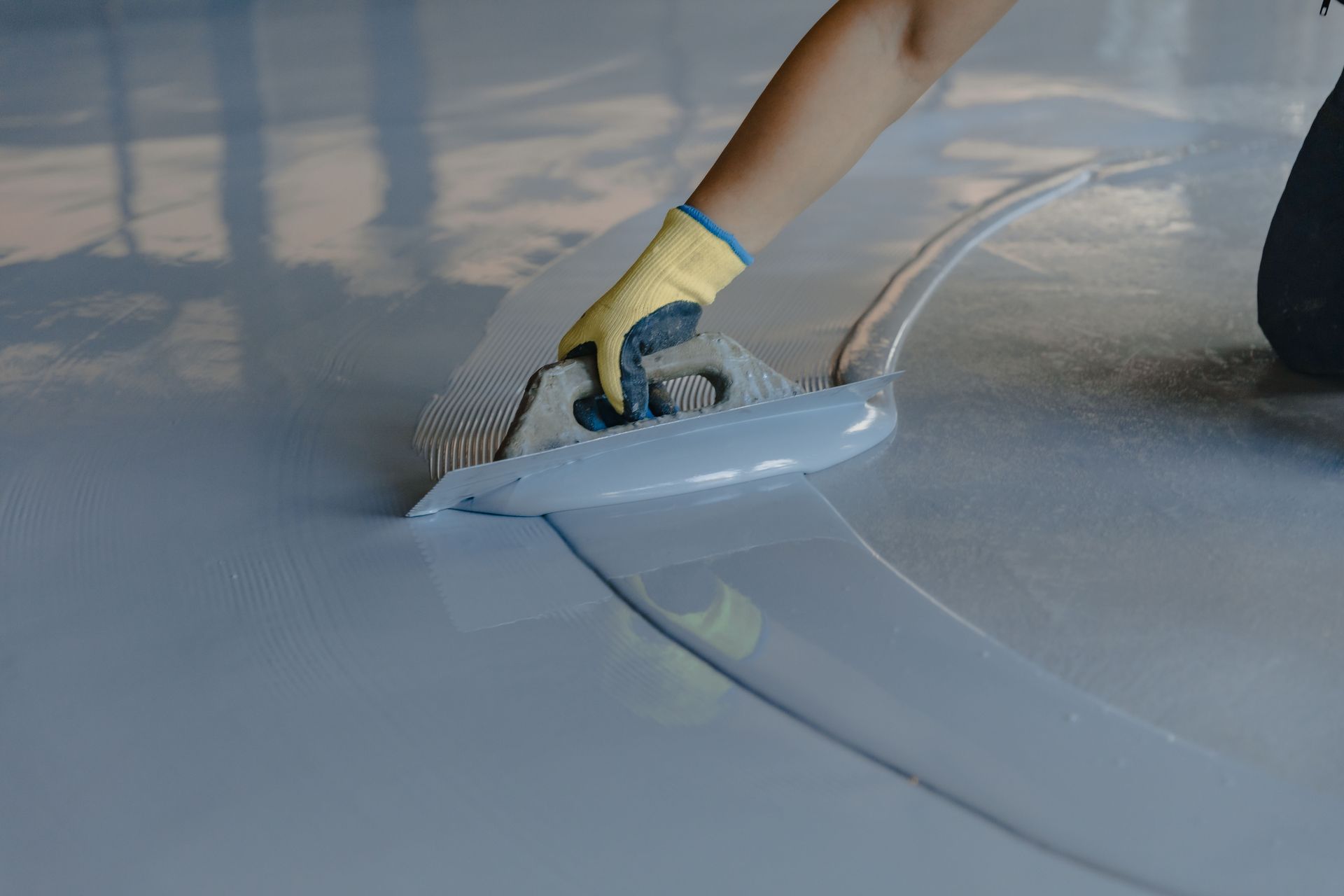 Person using a trowel to smooth a light grey epoxy coating on a floor.