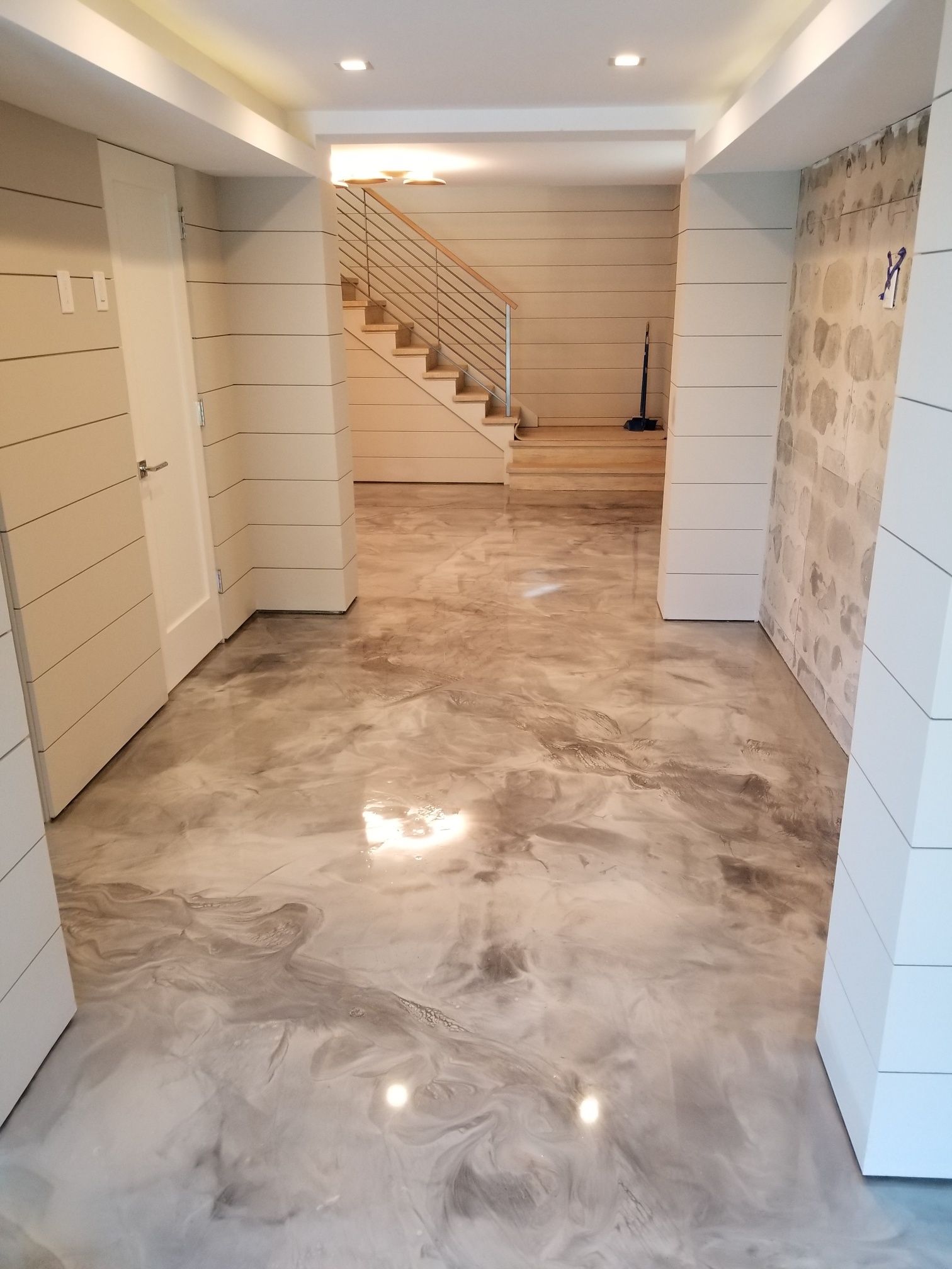 A hallway with a concrete floor and stairs in the background.