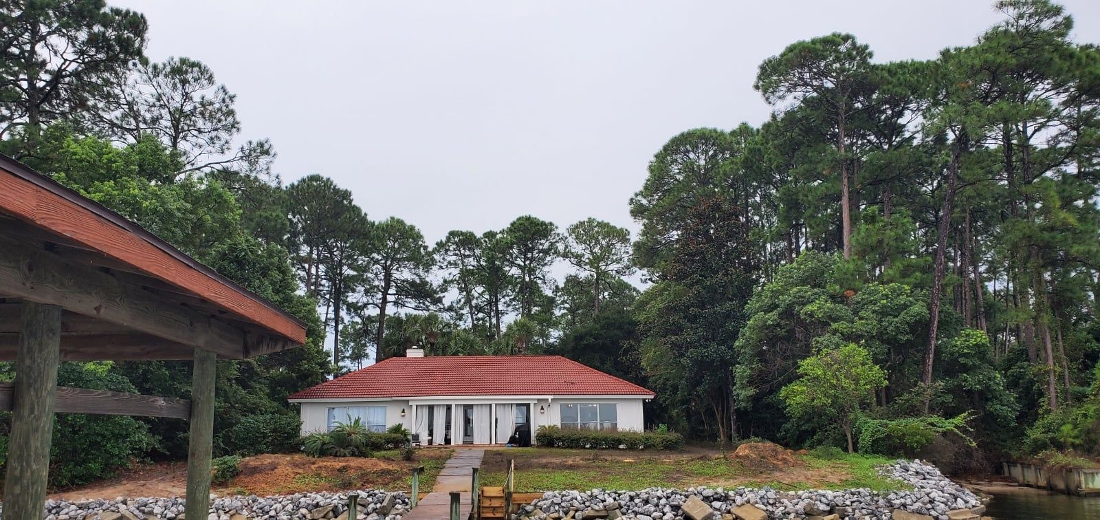 A house with a red roof is surrounded by trees and a body of water.