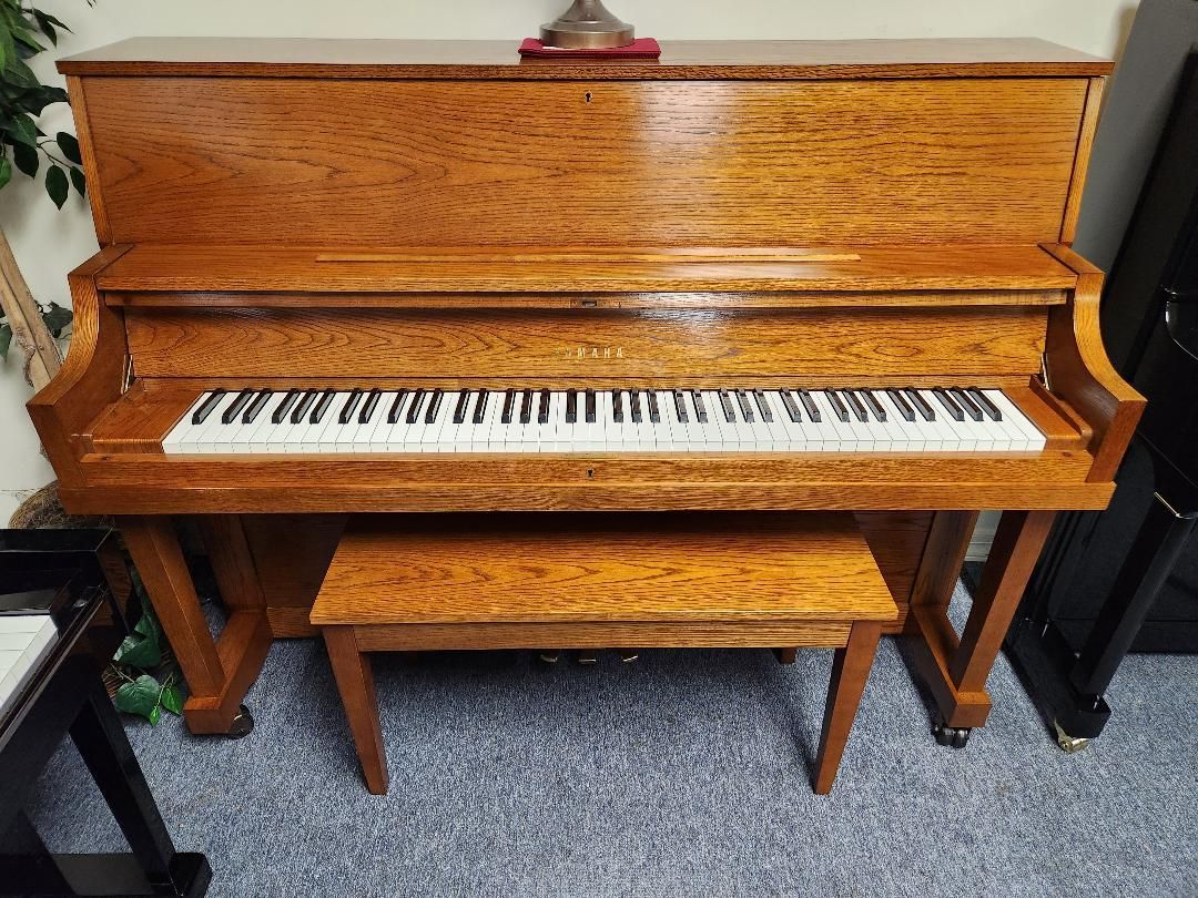 A wooden upright piano with a bench next to it in a room.