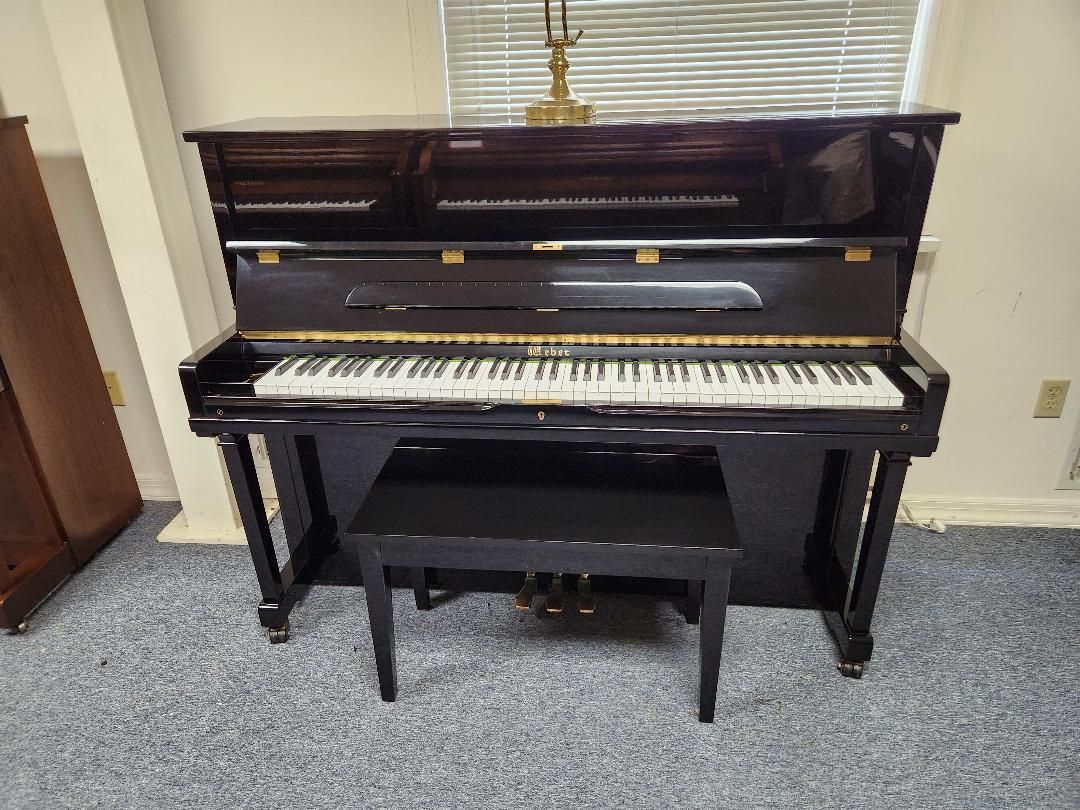 A piano is sitting in a living room next to a window.