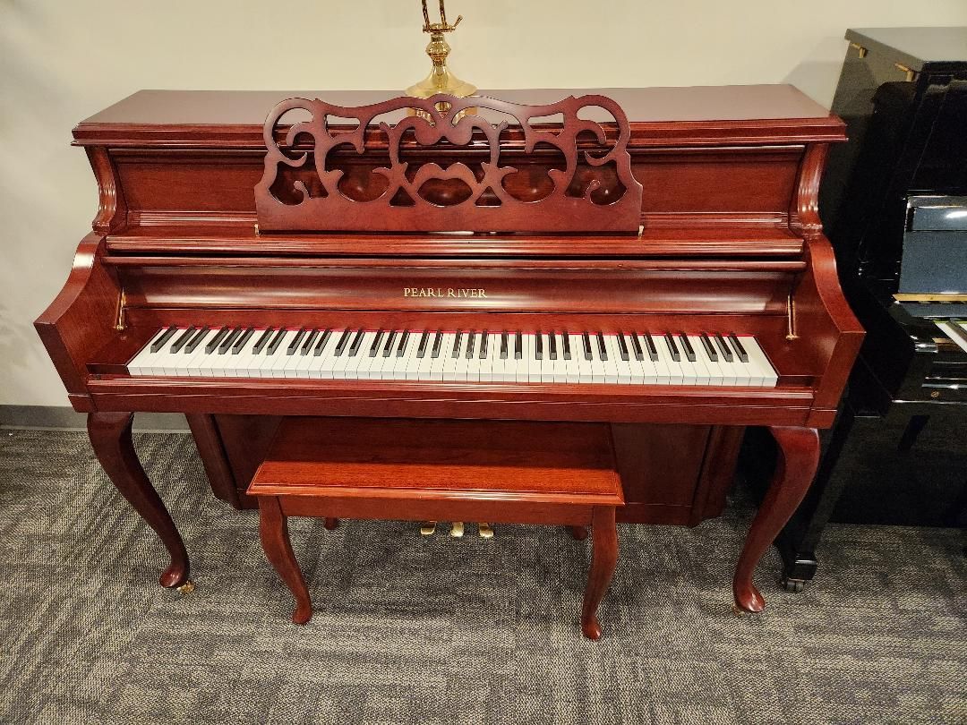 Red upright piano with a matching bench, music stand, and lamp.