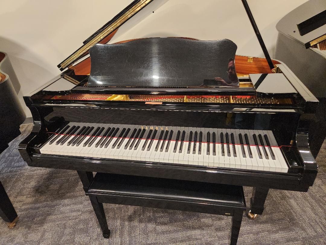 Black grand piano with its lid open, shown in a room from the front.